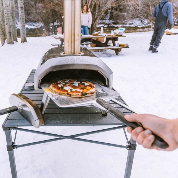 In the snow removing a pizza from an Ooni with a Pizza Peel